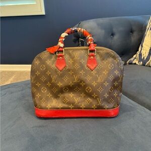 Authentic Louis Vuitton Alma Handbag. Nice red scarf rapped around the handles.